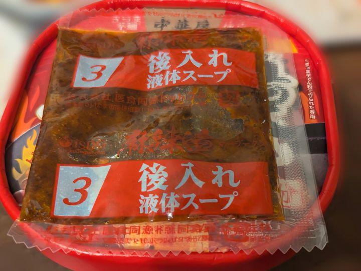 お湯を注いだ後、フタの上で液体スープの袋を温めている写真